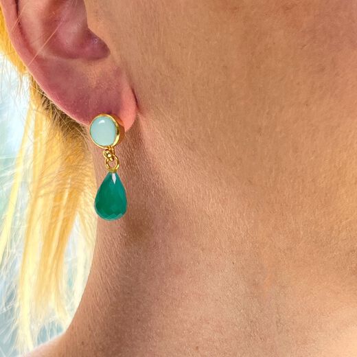 A woman with blonde hair wearing a drop earring with green stones.
